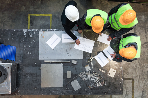 
Workers and manager in safety helmets working with documents at factory table